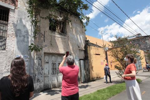 Técnicos estão diante de fachada de imóvel abandonado. #Paratodosverem