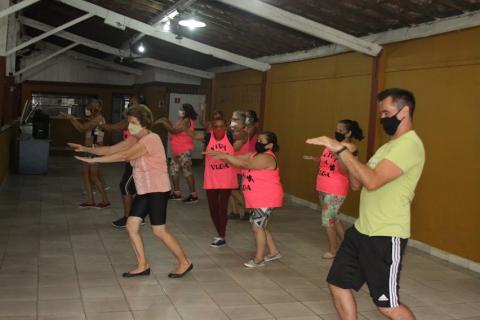 alunas estão de lado, com os braços esticados para frente, fazendo igual ao professor, em primeiro plano. #paratodosverem 