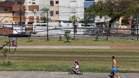 Linha do VLT com pessoas circulando na calçada ao lado e uma menina na bicicleta. #paratodosverem