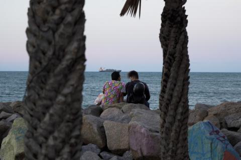 Dois homens estão sentados em pedras diante do mar. #paratodosverem