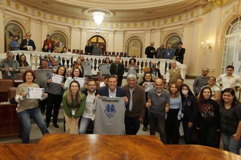 Voluntários e representantes da Prefeitura exibem camiseta e certificado. #paratodosverem