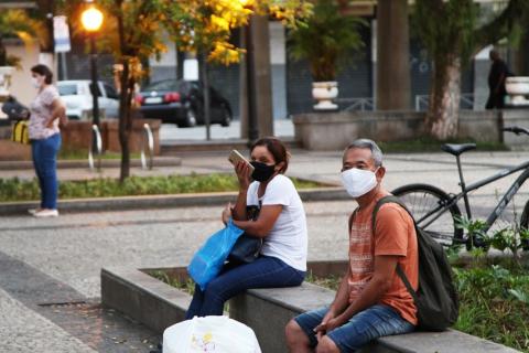 pessoas sentadas em praça de máscara #paratodosverem