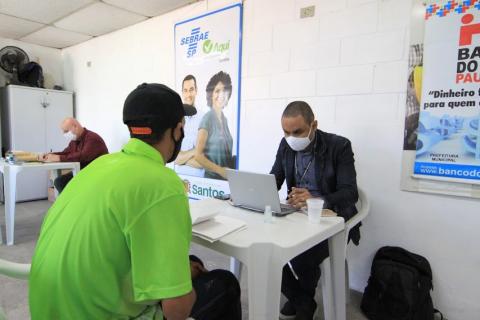 Rapaz está sendo atendido por outro homem, que está no computador. #paratodosverem