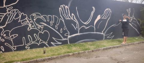 Artista desenha o grafite no muro preto. #paratodosverem