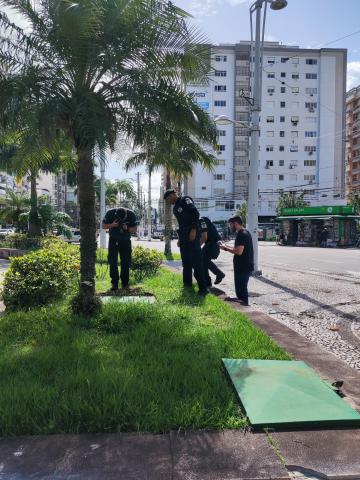 guardas olham caixa no jardim da praça #paratodosverem