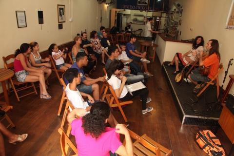 pessoas sentadas assistem pessoas em palco #paratodosverem