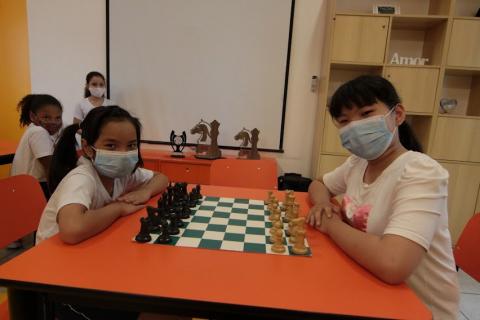 Elisa posa para foto ao lado da irmã, ambas diante de tabuleiro de xadrez. #paratodosverem