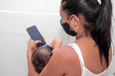 mulher com filho no colo olha pra celular #paratodosverem 
