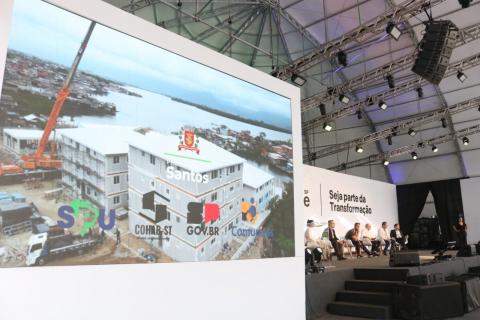 em primeiro plano, tela mostra obra e ao fundo os debatedores #paratodosverem