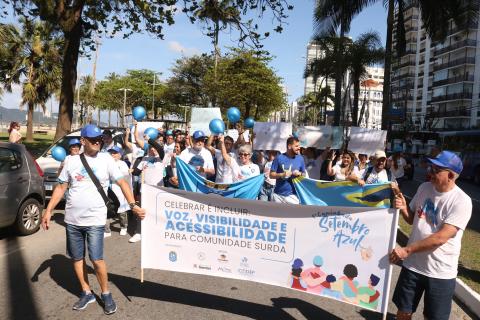 pessoas uniformizadas carregam faixa e cartazes na orla. #paratodosverem