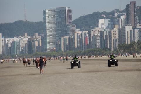Guardas percorrem com triciclos a faixa de areia. Há pessoas caminhando. #Paratodosverem