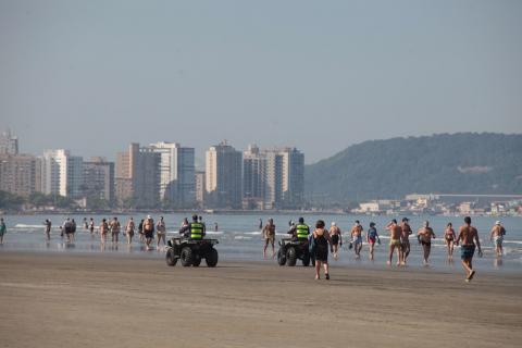 Guardas circulam de quadriciclos trecho de faixa de areia. Há pessoas caminhando. #Paratodosverem