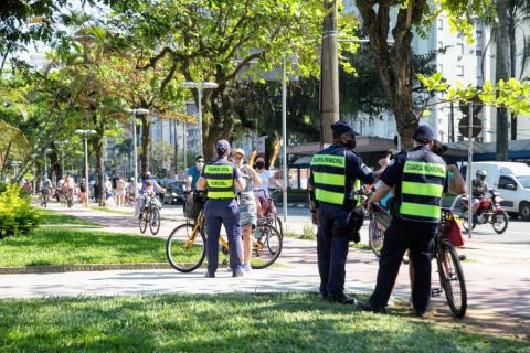 Guardas estão no jardim da orla, junto à ciclovia conversando com ciclistas. #Paratodosverem