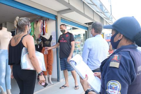 Fiscal e guarda municipal estão na porta de estabelecimento falando com um homem. #Paratodosverem