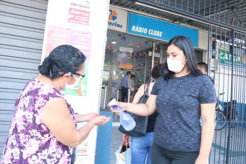 Mulher borrifa álcool em gel nas mãos de outra mulher. #Paratodosverem