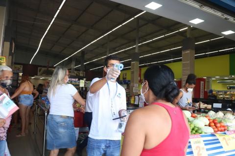 Homem na entrada de loja de frutas mede a temperatura de mulher. #Paratodosverem