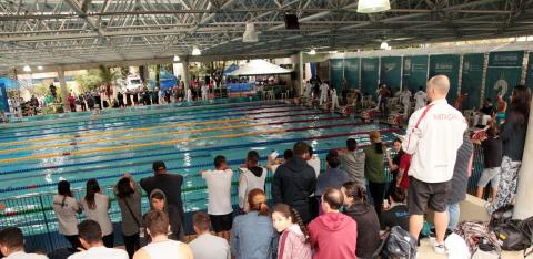 Piscina com pessoas nadando e público assistindo. #Pracegover