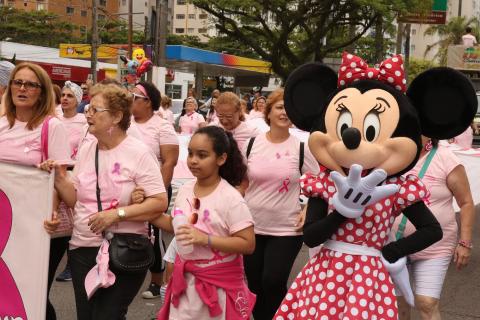 pessoas caminham ao lado de pessoa vestida como minnie #pracegover