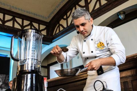 Chefe de cozinha adiciona pó de café a uma frigideira. À frente dele há um liquidificador. #Pracegover