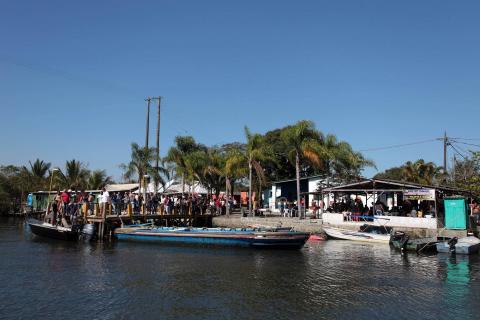 #pracegover Cerca de 40 pessoas aquardam em plataforma para embarque em pequeno barco