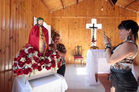 #pracegover Mulher fotografa idosa junto a estátua de Jesus dentro de igreja