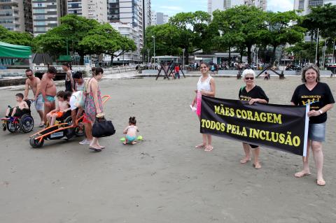 Na areia da praia, três mulheres estendem o cartaz com o dizer 
