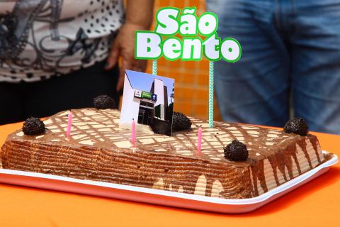 Bolo de aniversário com decoração na parte superior onde se lê São Bento. #Pracegover