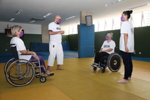 duas alunas cadeiranes olham para professor #paratodosverem