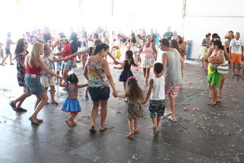 Crianças dançam em matinê em tenda. Muitas delas participam de uma roda com adultos. #Paratodosverem