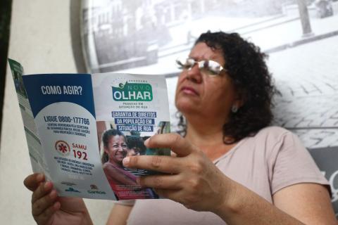 Mulher lê folder com informações sobre o programa Novo Olhar. #Pracegover