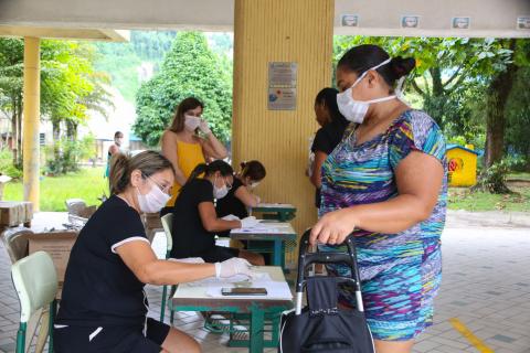 mulher se aproxima de mesa onde há lista #paratodosverem 