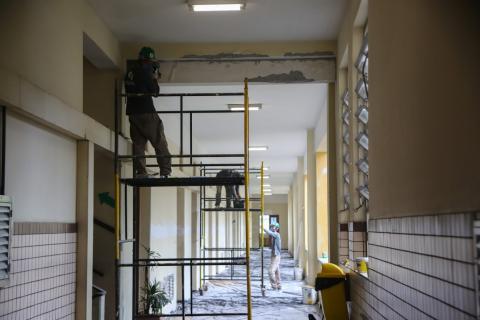 HOmens trabalham em obras em corredor interno. Dois deles estão em andaimes. #Paratodosverem