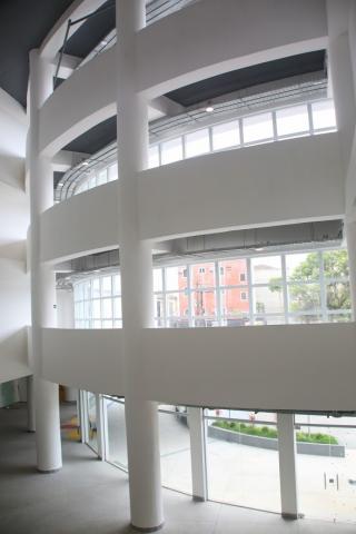Área interna do prédio, com vista de três andares em curva convexa, sustentada por colunas. #Paratodosverem