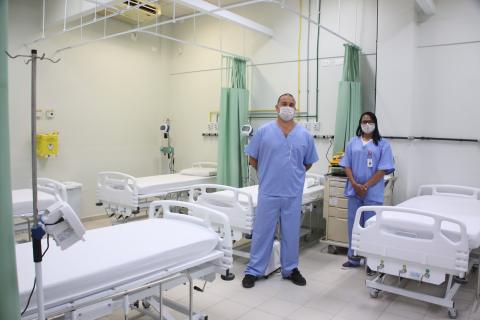 Sala de enfermaria com cinco macas. Há duas pessoas em pé usando máscaras. #Paratodosverem