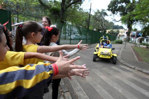 meninas estendem a mão para atravessar em faixa na minipista, enquanto bugue se aproxima #pracegover 