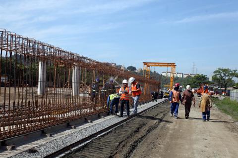 operários caminhando ao lado da obra #pracegover 