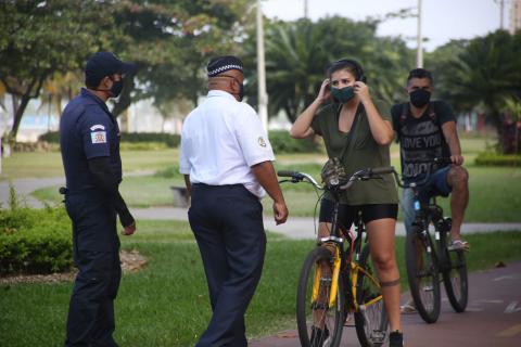 #pracegover Na ciclovia da orla, dois guarda municipais mascarados abordam mulher e homem também mascarados sobre bicicletas