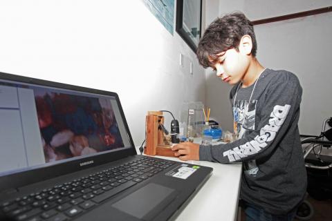 menino está ao lado de computador #pracegover 