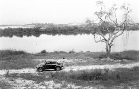 Imagem antiga com fusca e mulher, parados próximos a área do Dique da Vila Gilda. #pracegover