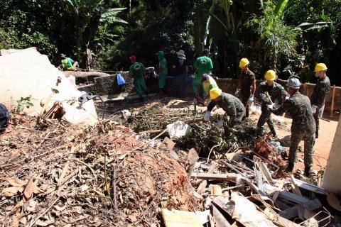 Homens do Exército e prefeitura fazem limpeza em terreno. Há grande volume de galhos e madeiras. #paratodosverem