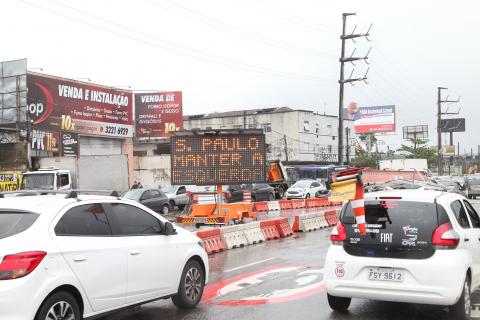 Pista em primeiro plano com veículos de costas para a imagem. Há separadores na pista e um painel luminoso onde se lê S.Paulo Mantenha a Esquerda. #Paratodosverem