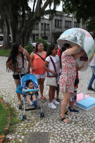 Pessoas fazem fila próximo a orelhão estilizado. #Pracegover