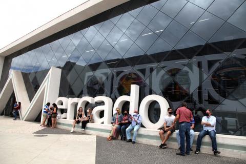 Fachada do novo Mercado de Peixes com pessoas sentadas à frente. #pracegover