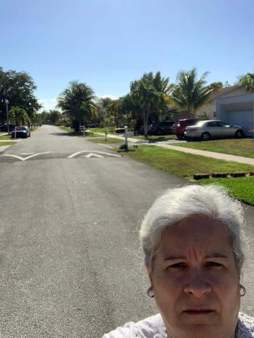 Mulher tira selfie em rua vazia. A calçada, ao lado direito da foto, é gramada. #Paratodosverem