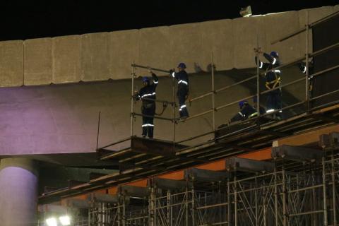 Operários uniformizados e com faixas reflexivas no uniforme, porque trabalham à noite, removem estrutura sob viaduto. #Paratodosverem