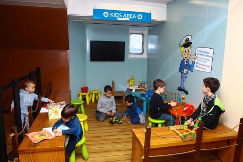 Espaço para criatividade infantil na embarcação. Há crianças desenhando e pintando sobre pequenas mesas. #Pracegover