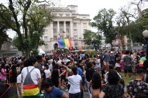 Vista geral da Praça Mauá lotada de pessoas. Bandeira da causa LGBT está pendurada na frente da Prefeitura. #Pracegover