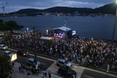 Grande público cerca palco defronte para o mar. Foto foi feita à noite. #Pracegover
