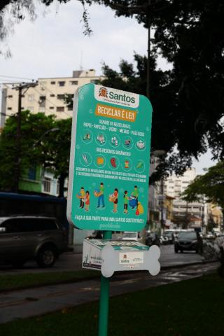 Painel com display para distribuição de embalagem para fezes de animais. Na parte superior há um painel com propaganda. #Pracegover