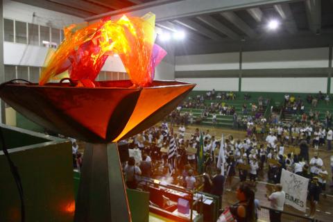 tocha acesa com pessoas da cerimônia de abertura ao fundo #pracegover 